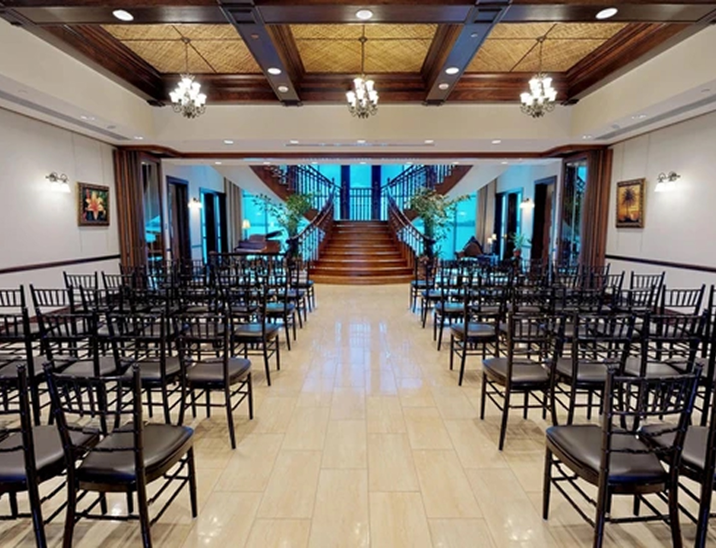 Ceremony setup with black chairs, elegant chandeliers, and a grand wooden staircase at Tavares Pavilion on the Lake