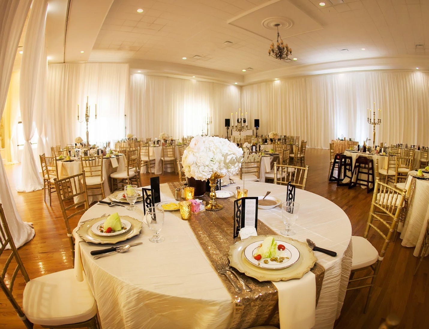 Elegant wedding reception at The Regent with gold chiavari chairs, white draping, and floral centerpieces on round tables
