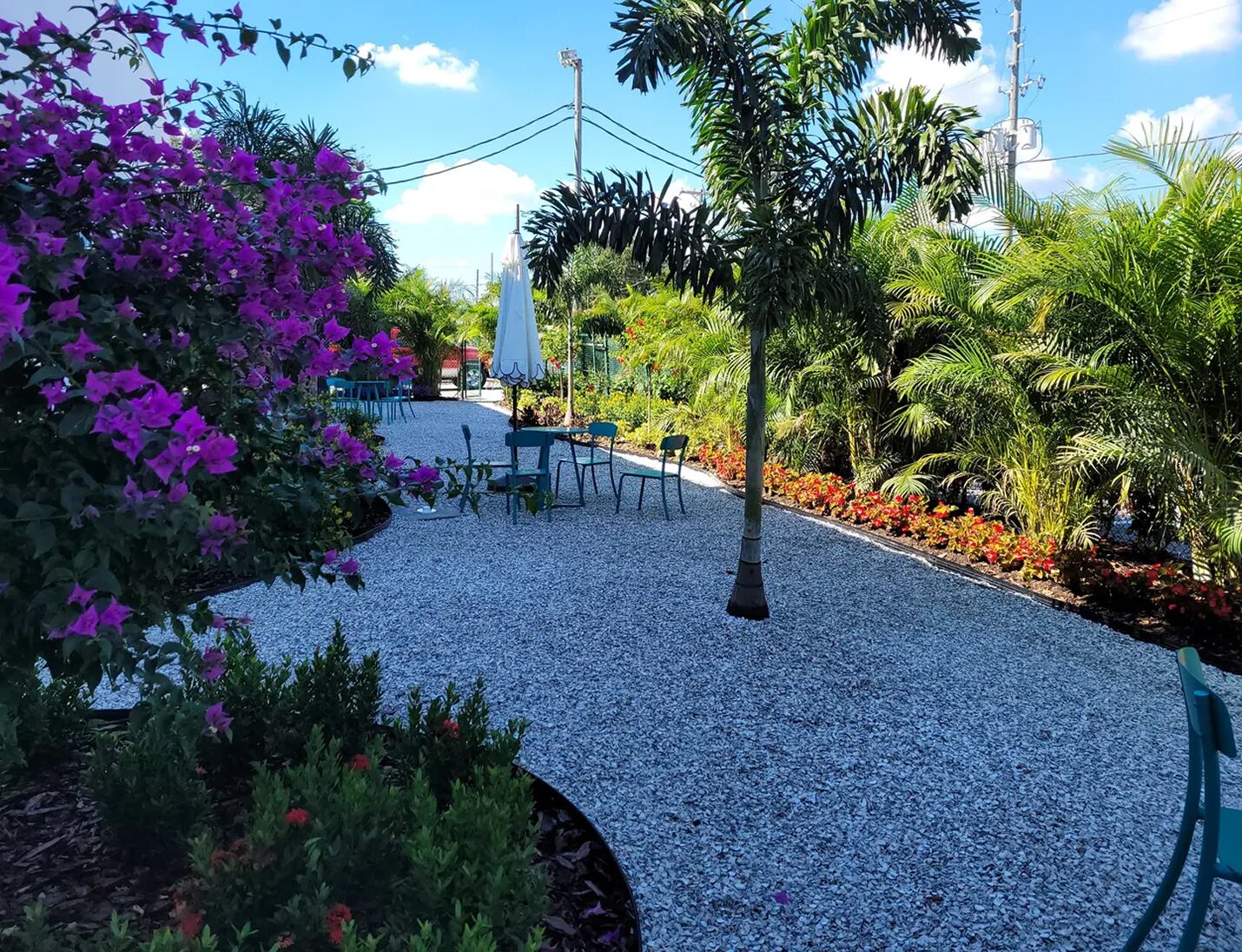 Outdoor garden seating area at The Factory St. Petersburg with palm trees, flowering plants, and gravel pathways