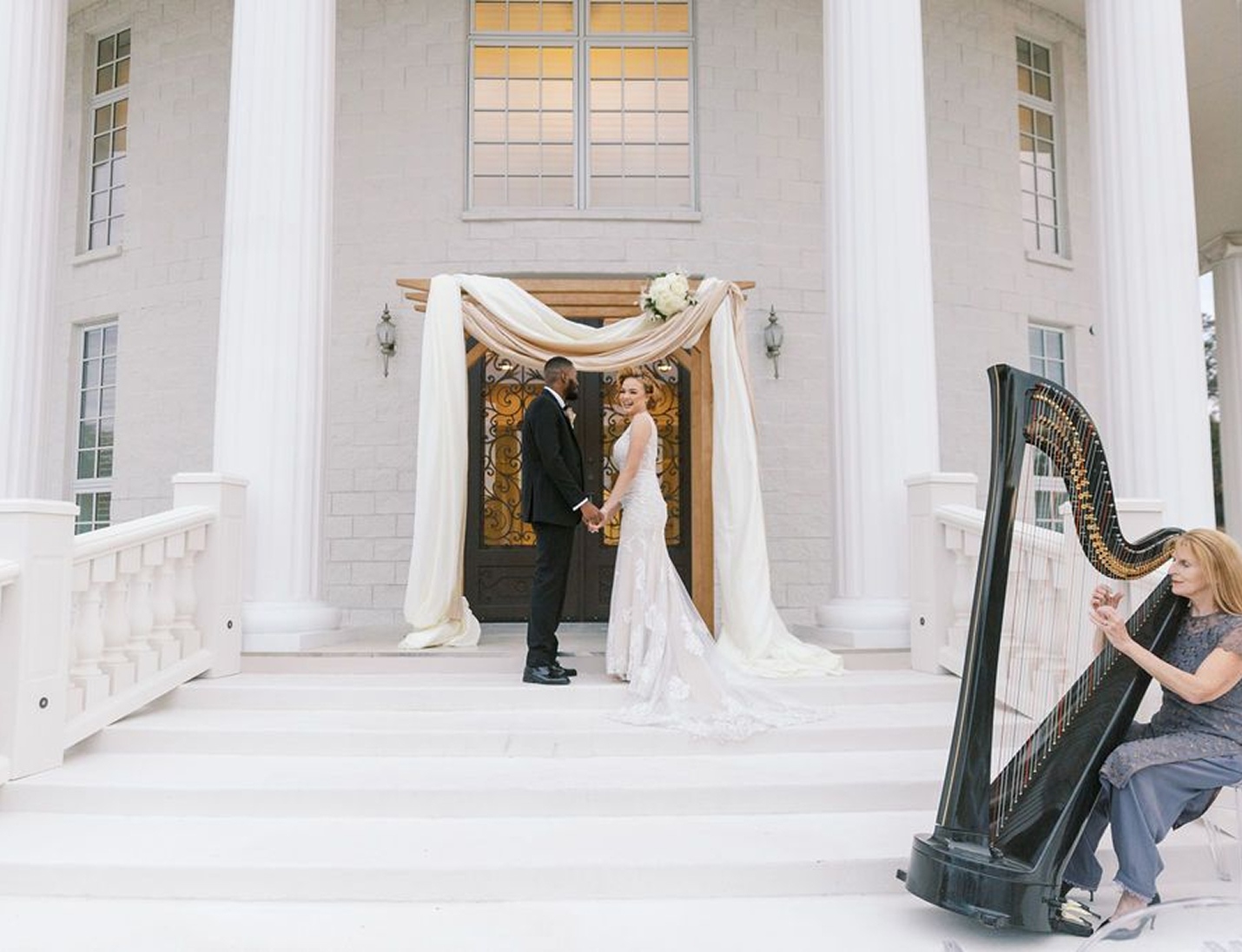 Wedding couple standing on the grand white steps of Whitehurst Gallery with elegant columns and a harpist performing