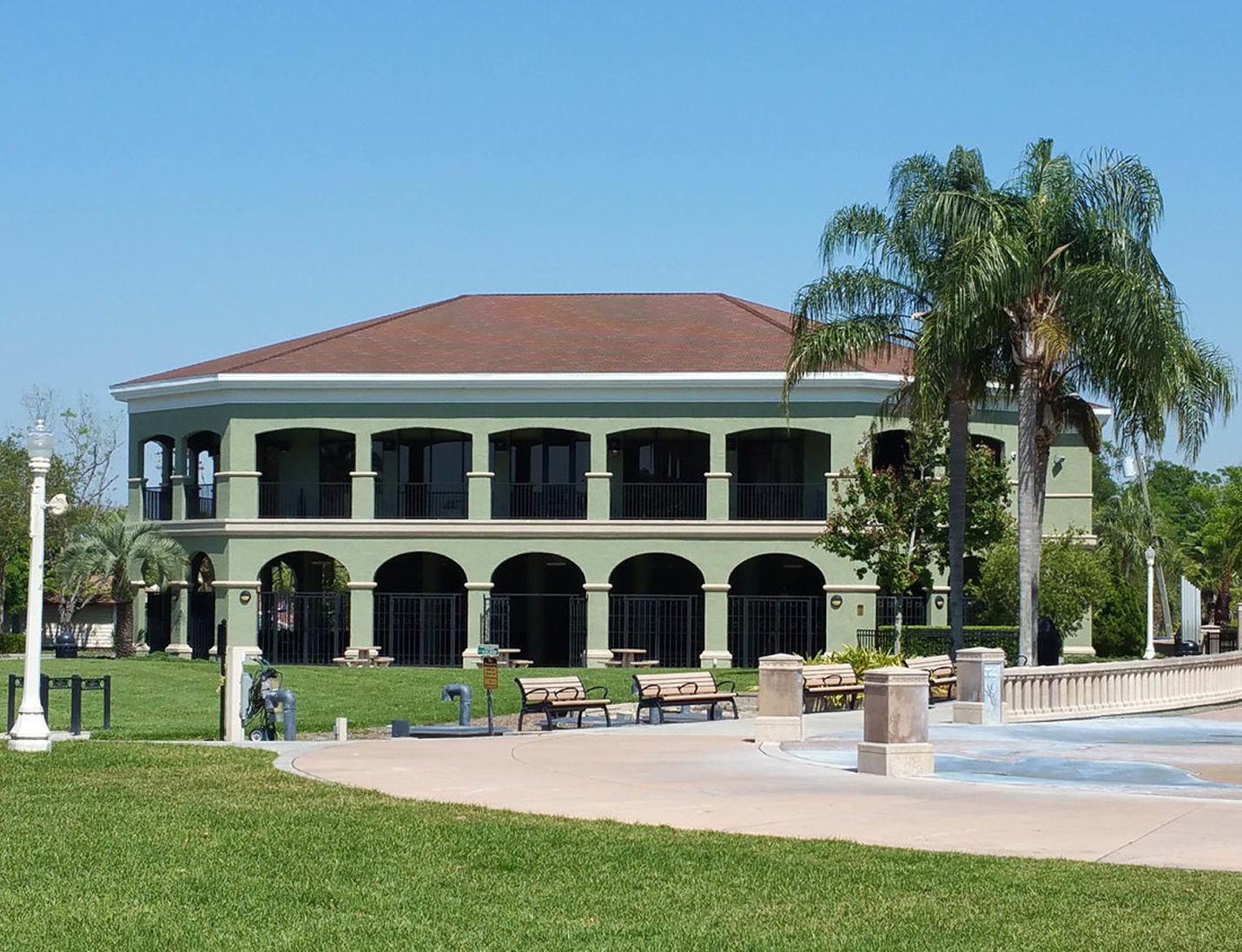 Exterior of The Peggy Brown Building with green facade, arched walkways, palm trees, and an open lawn area in front