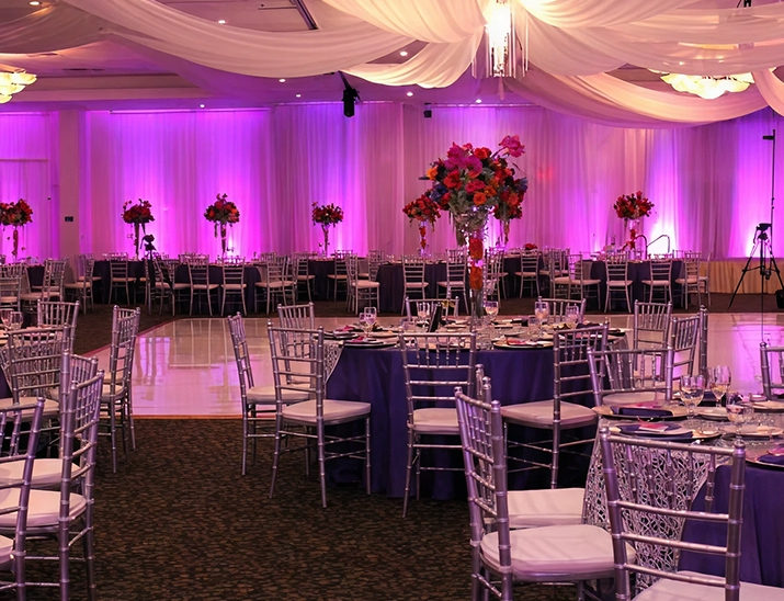 Elegant reception setup at Bayanihan Arts and Events Center with purple uplighting, draped ceiling and silver chairs
