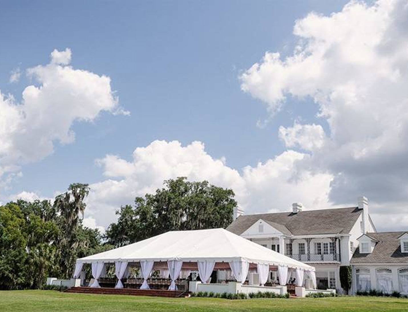 Elegant tented wedding setup at Adam’s Estate with white drapery and manicured lawn in front of the manor