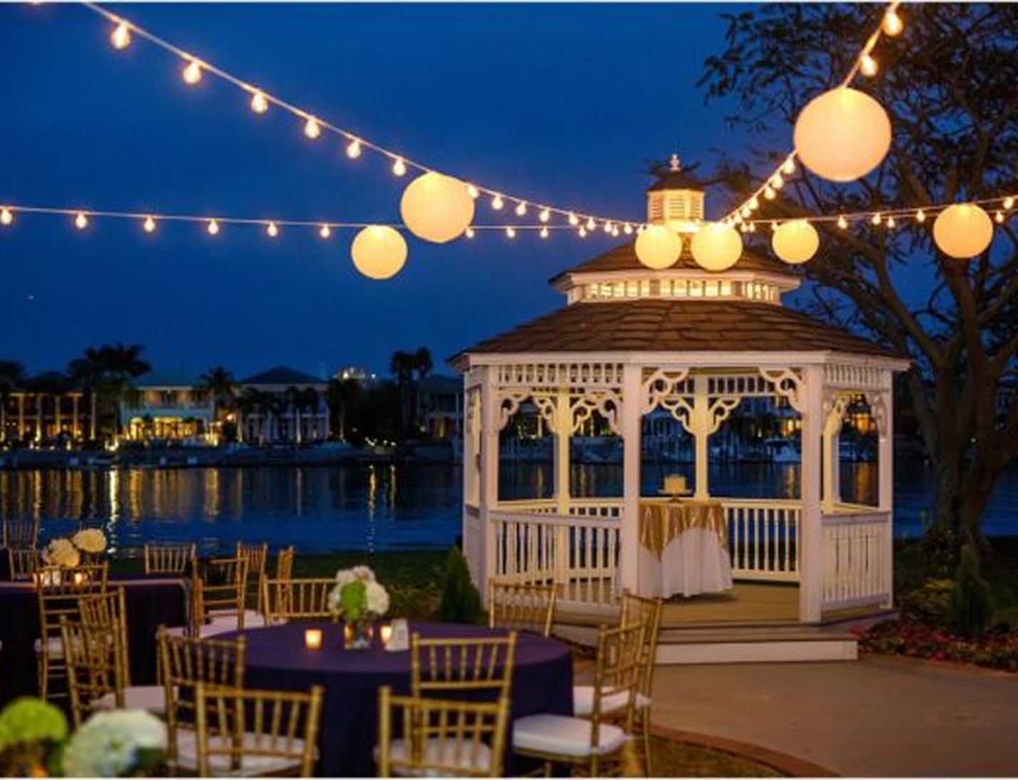 Evening waterfront setup at Davis Islands Garden Club, featuring a lit gazebo, string lights, and elegant table settings