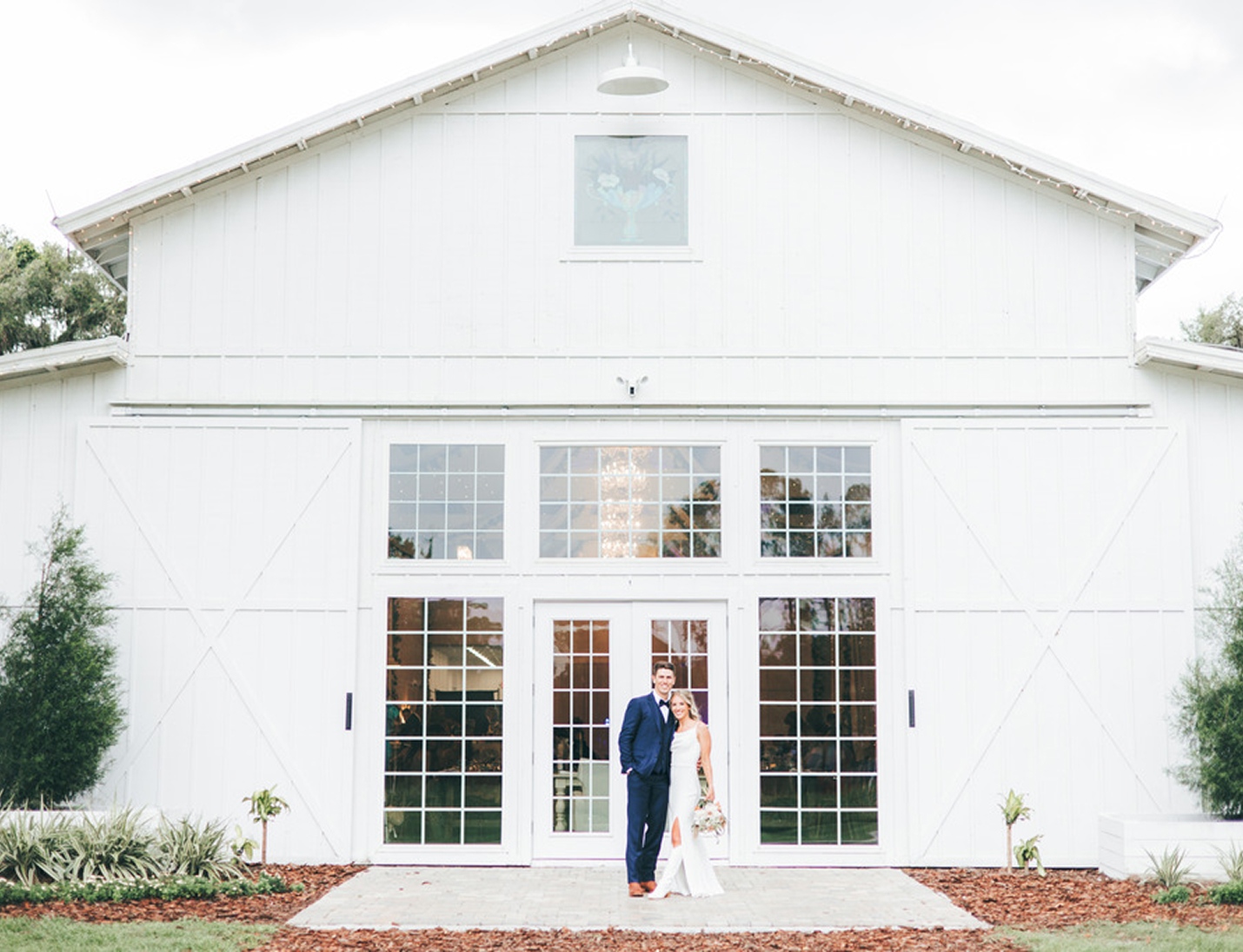 Bride and groom standing in front of the elegant white barn venue at Ever After Farms, posing for wedding portraits