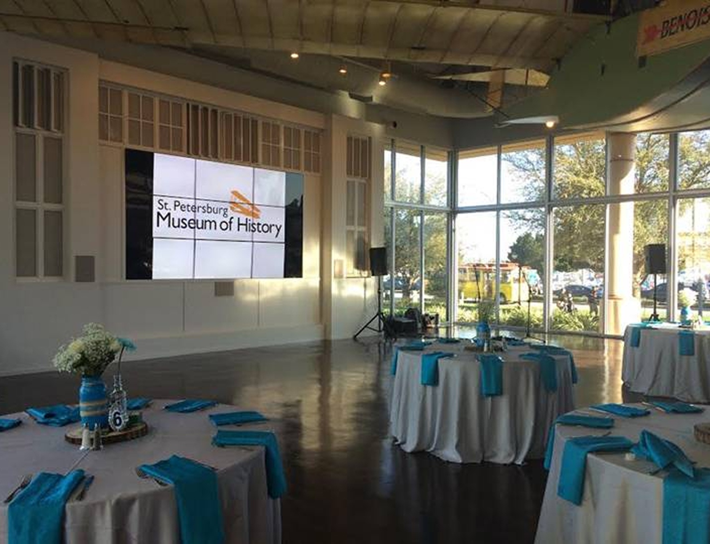 Event setup at St. Petersburg Museum of History with round tables, blue napkins, and large windows with natural light