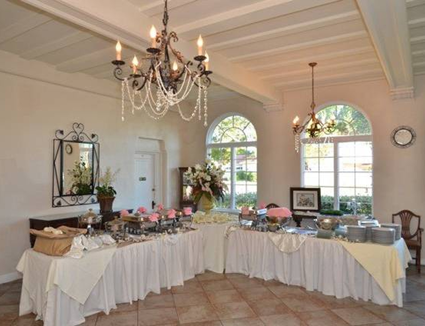 Buffet setup with white linens and chandeliers inside St. Petersburg Women’s Club, with elegant decor and arched windows