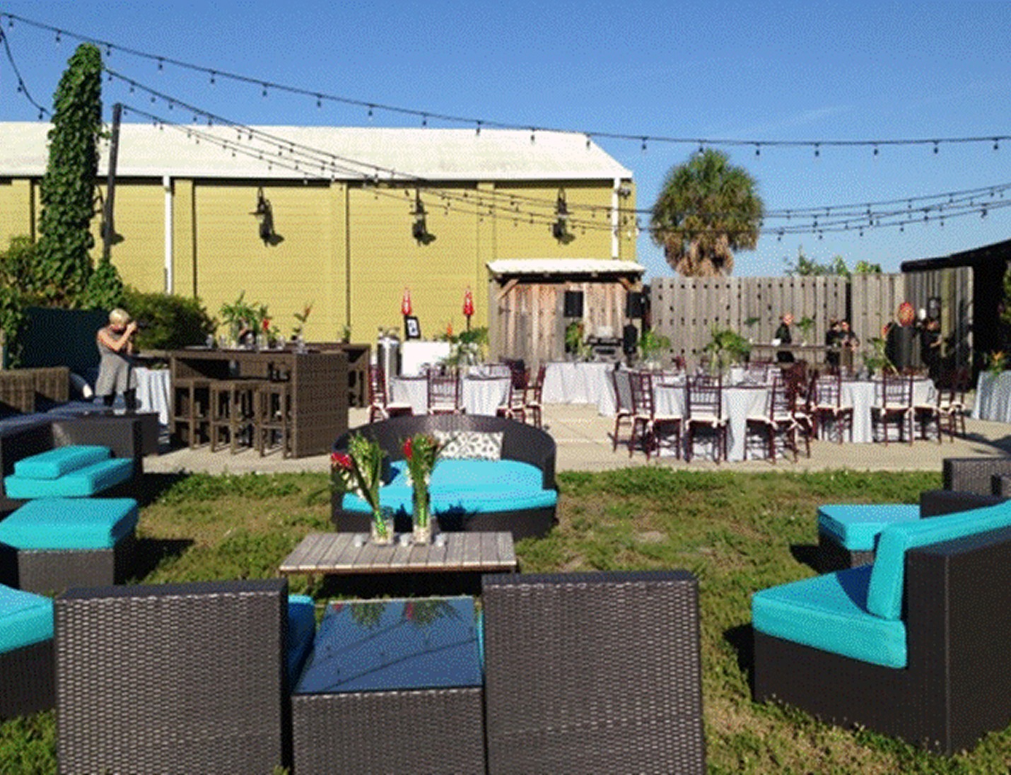 Outdoor event setup with wicker lounge seating, turquoise cushions, and string lights at Duncan McClellan Gallery