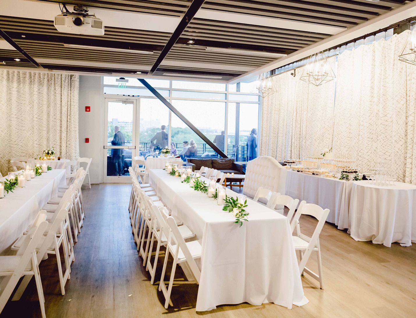 Rooftop 220 event space with long white tables and chairs, greenery centerpieces, and large windows overlooking the view