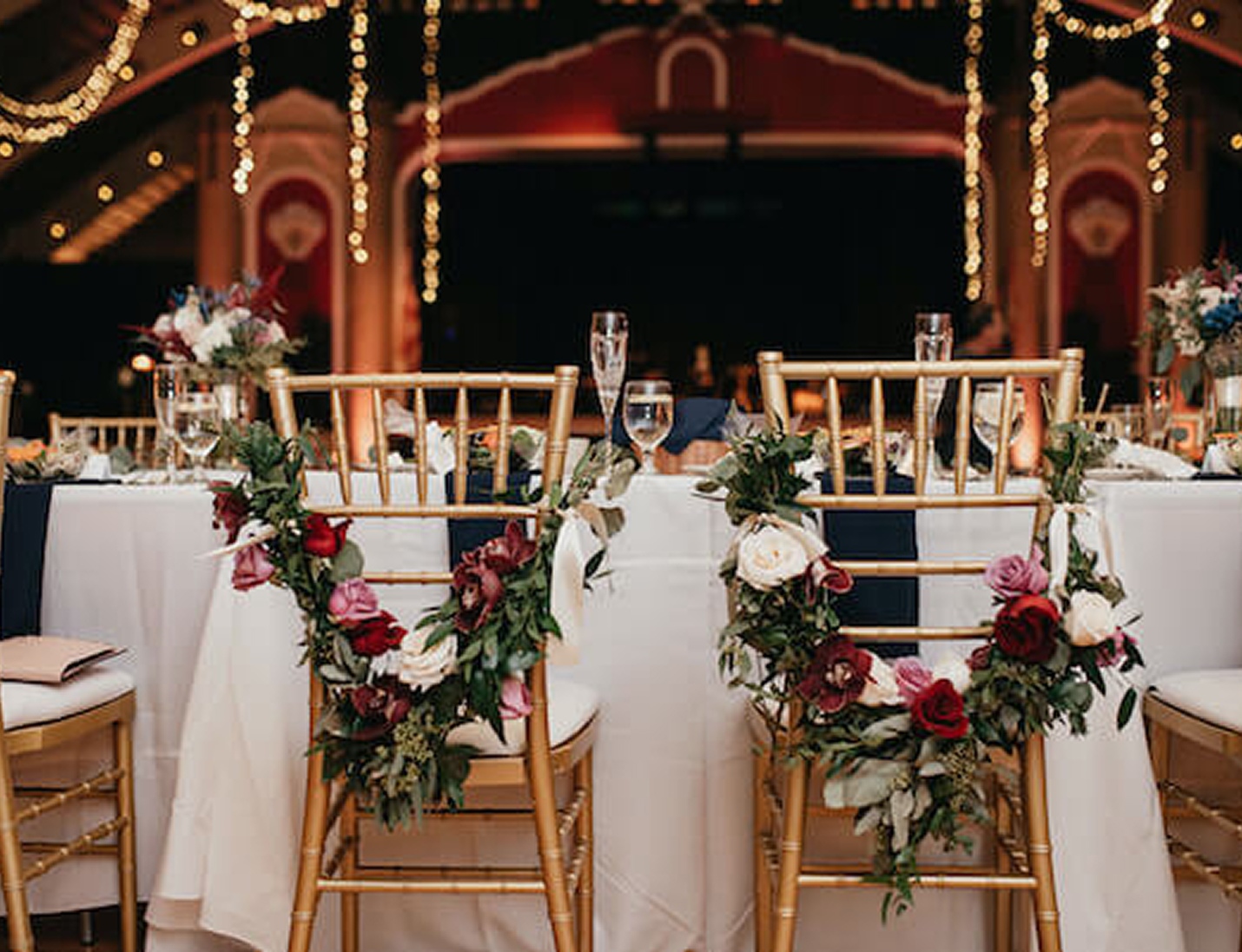 Decorated round table at The Coliseum St. Petersburg with gold chairs, floral chair garlands, and warm string lights