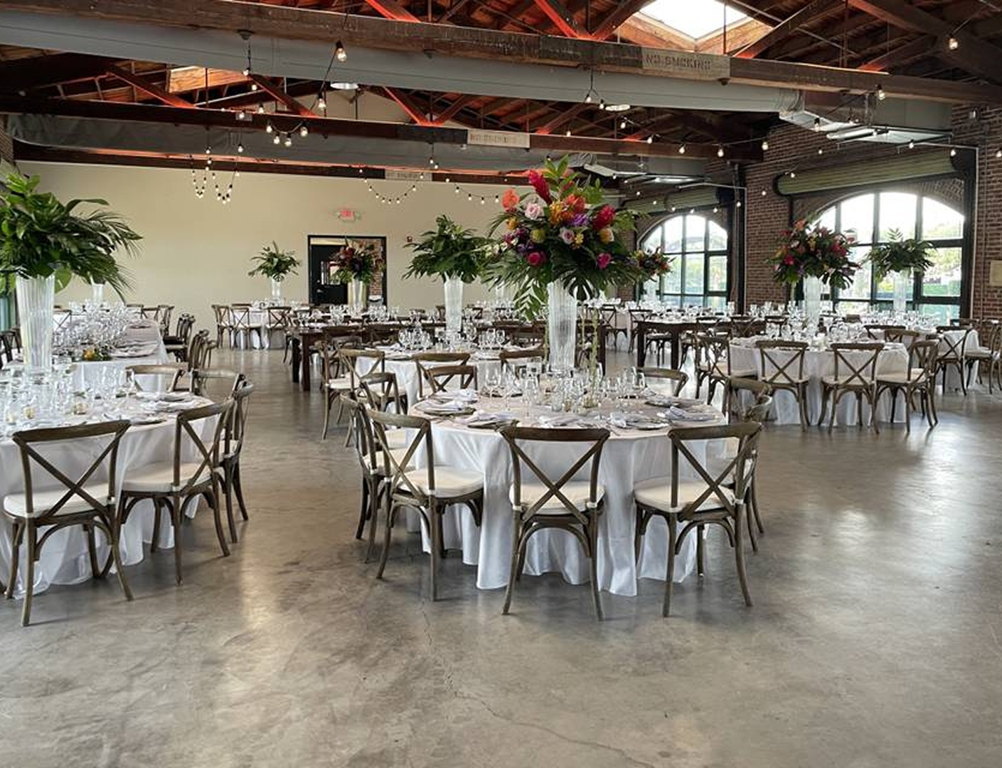 Wedding reception setup at Morean Center for Clay with round tables, wooden chairs, and tall floral centerpieces
