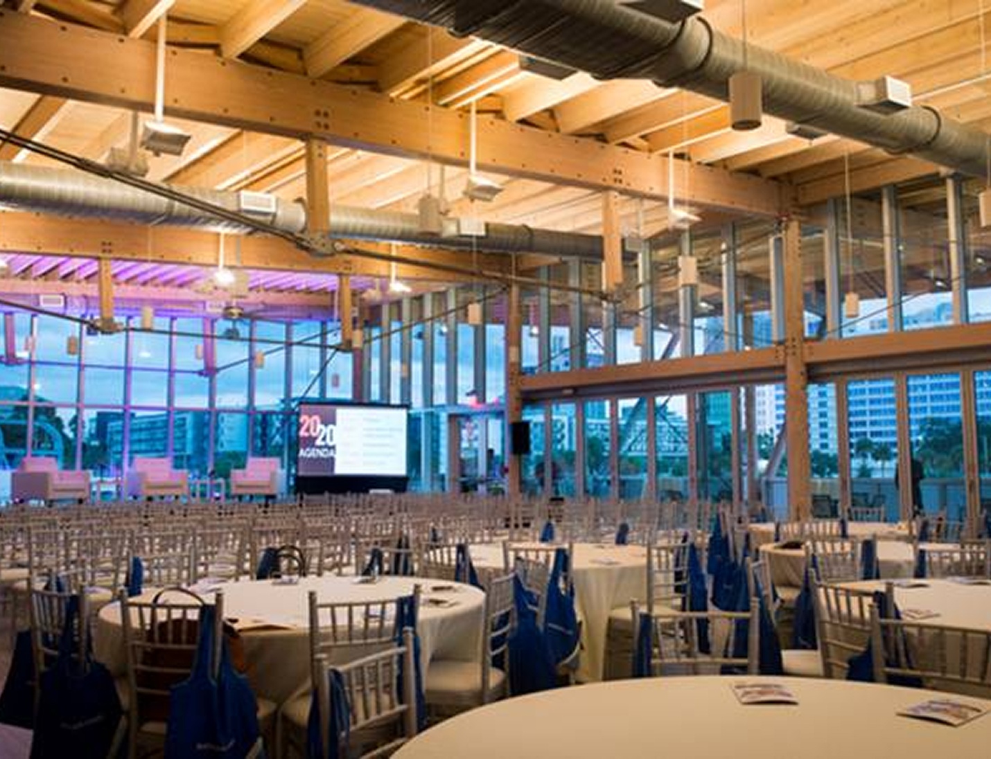 Modern glass-walled event space with round tables and a city view at Tampa River Center
