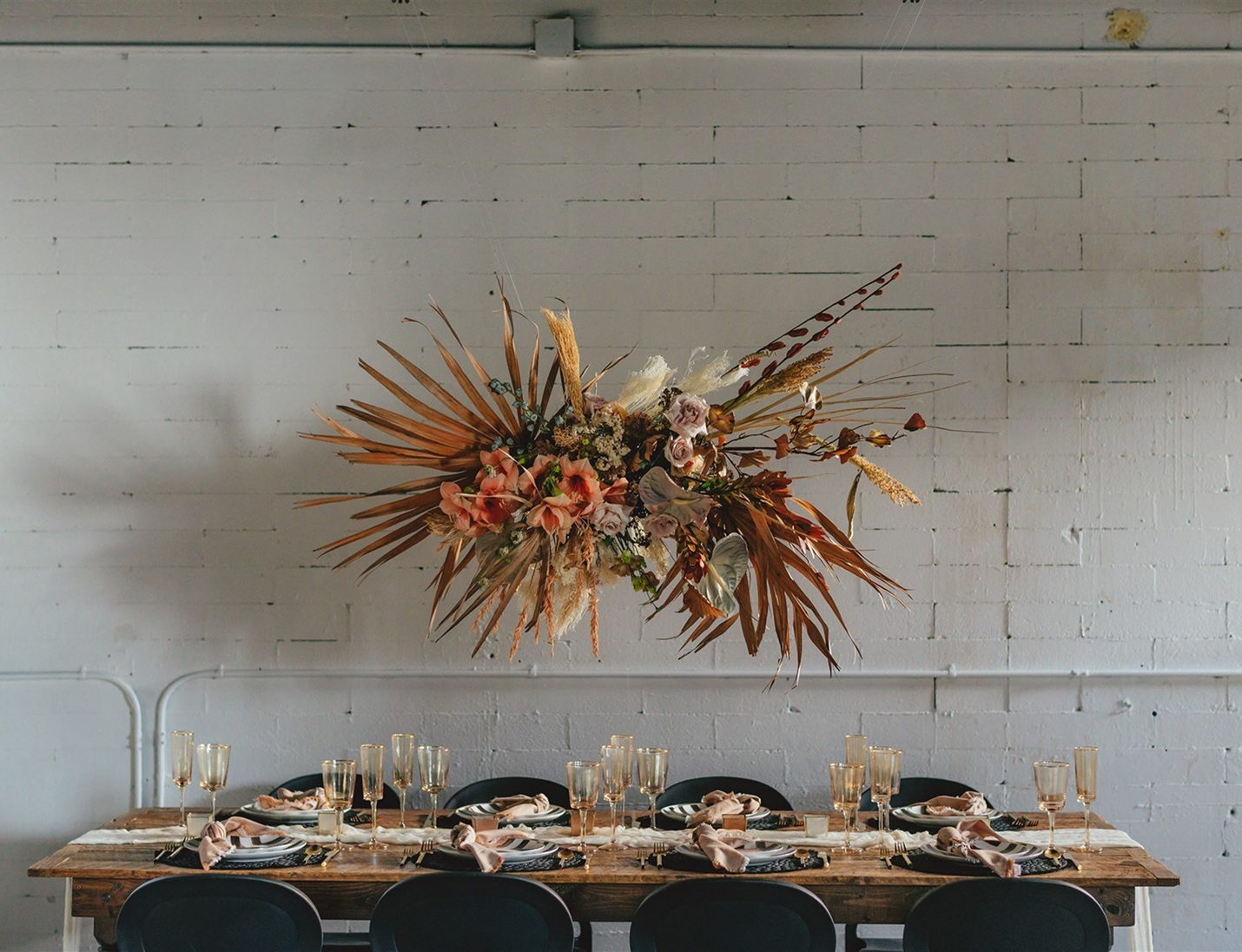 Modern space with a rustic table set for dinner, a dried floral arrangement, and a white brick wall at The West Events