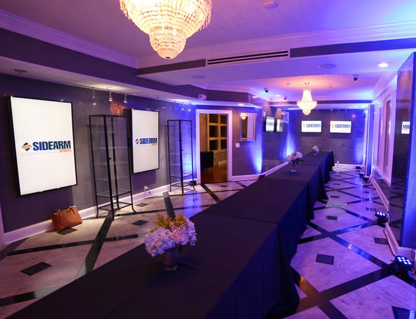 Event setup at Penthouse 450 with long black-draped tables, digital display screens, chandeliers, and blue uplighting