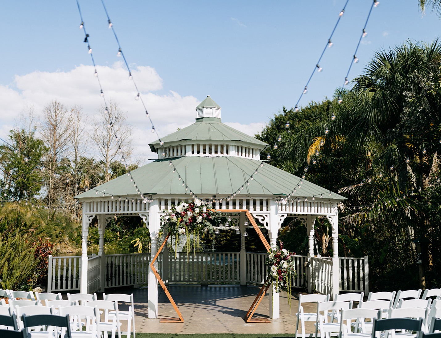 Wedding setup at Mixon Fruit Farms featuring a white gazebo, floral arch accents, white chairs, and string lights overhead