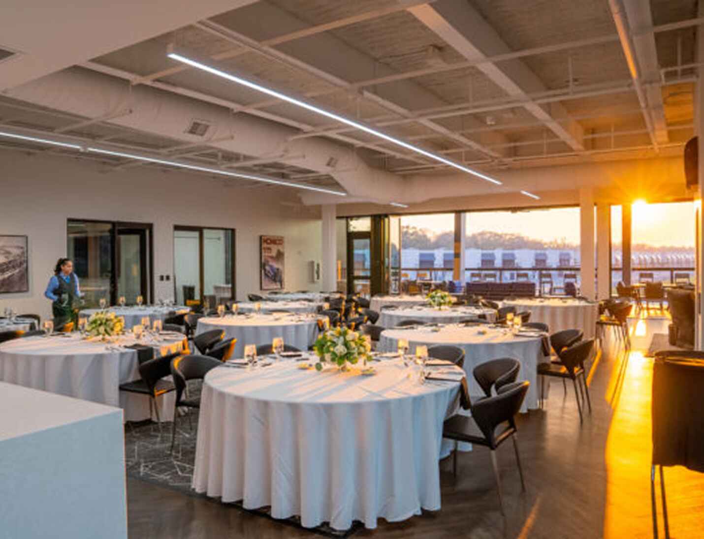 Elegant event setup at The Motor Enclave with round tables, modern chairs, and warm sunset light through large windows