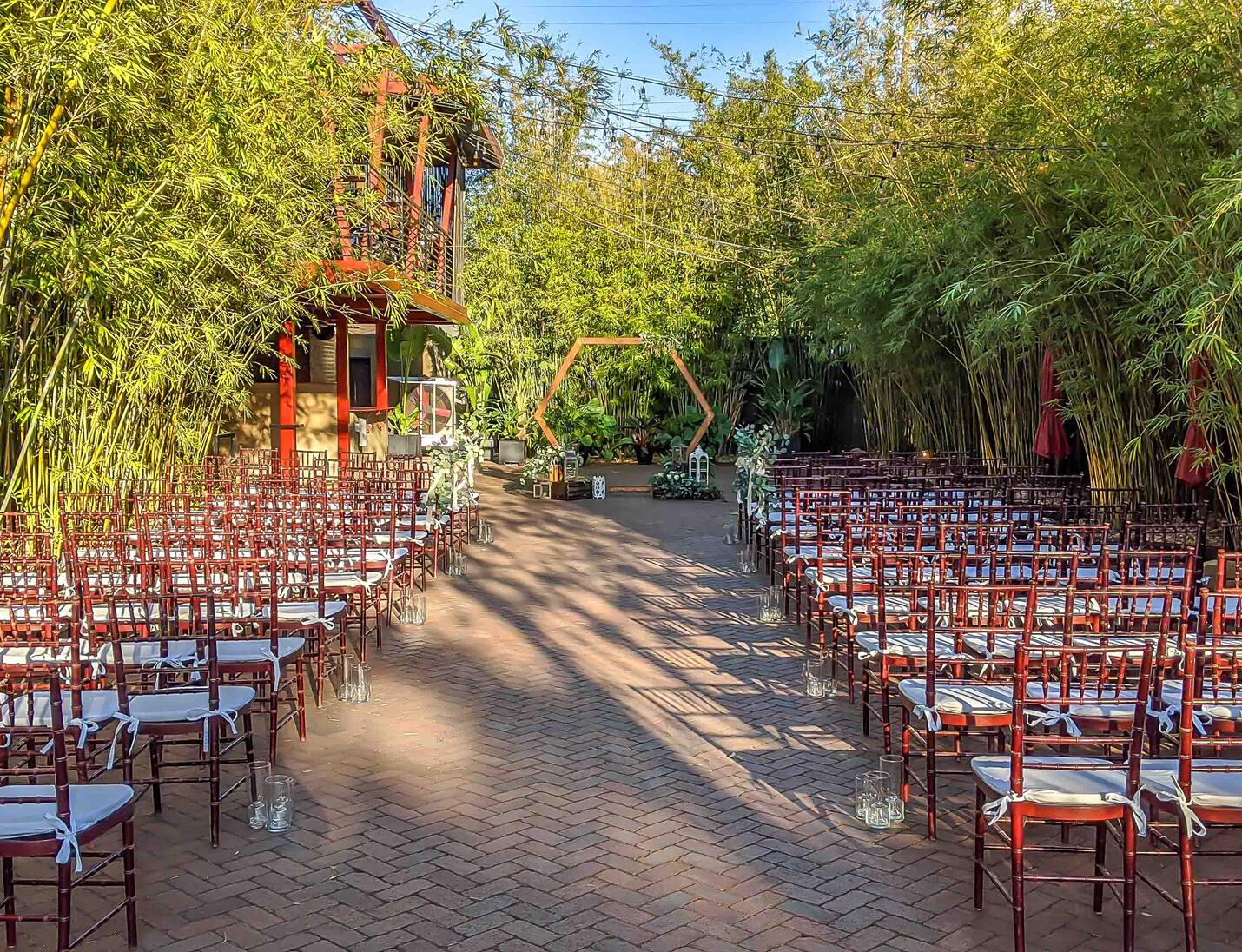 Outdoor ceremony setup at Nova 535 surrounded by tall bamboo, wooden chairs, and a geometric arch at the aisle front