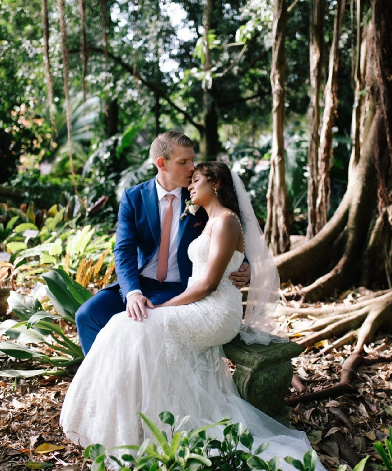 Bride and groom sharing a tender moment surrounded by lush greenery and large roots at USF Botanical Gardens
