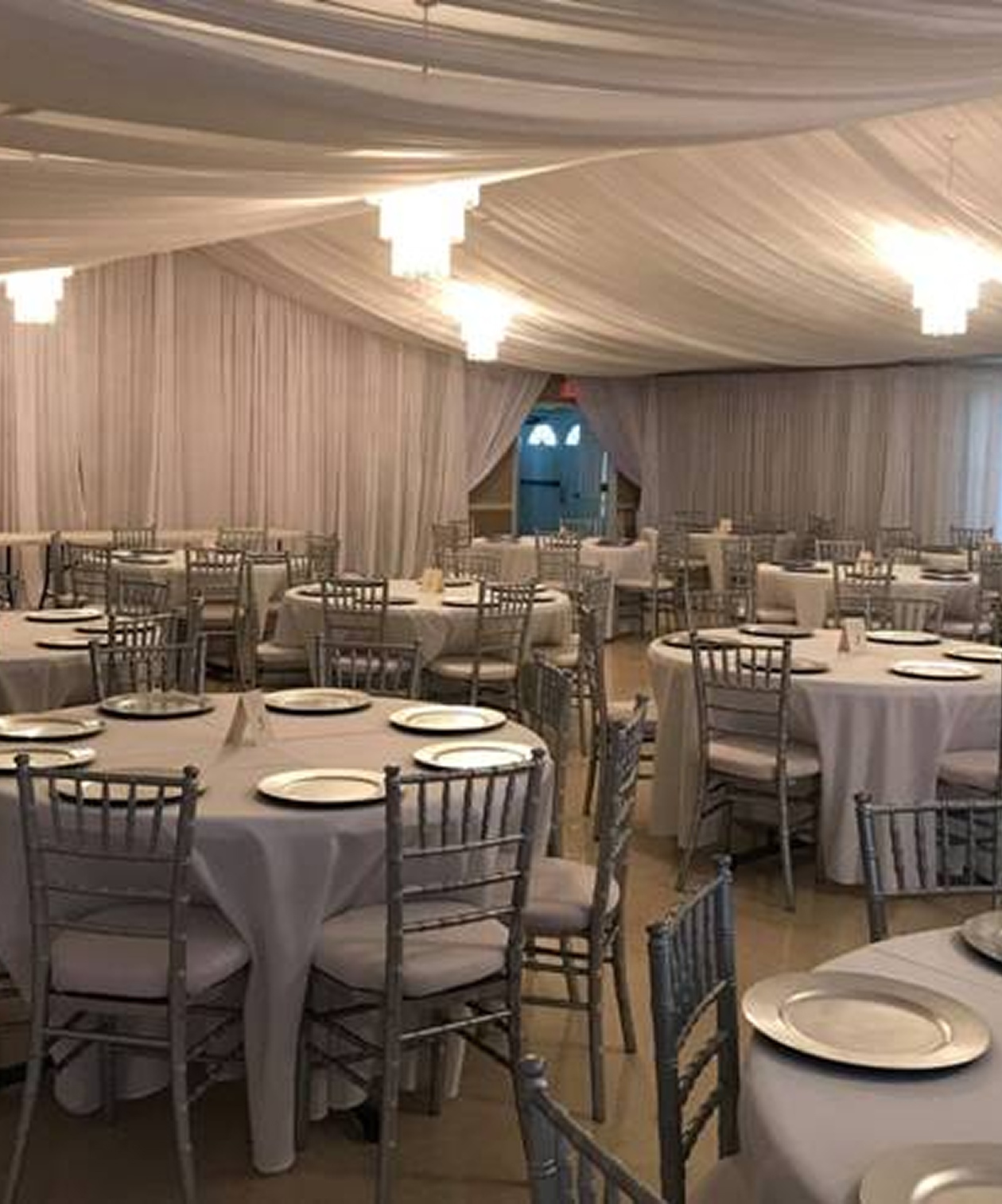 Elegant banquet setup with silver chairs, draped white ceiling, and round tables at GFWC Tampa Women’s Club