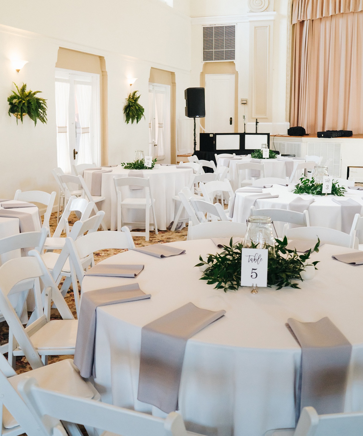 Bright reception hall setup with white chairs, round tables and greenery centerpieces at St. Petersburg Women’s Club