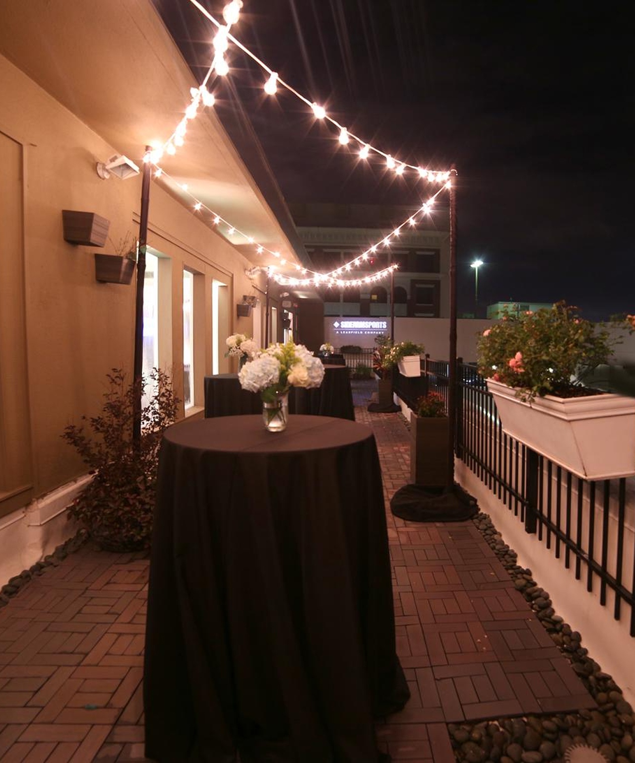 Outdoor terrace setup with black cocktail tables, string lights, and floral arrangements at Penthouse 450