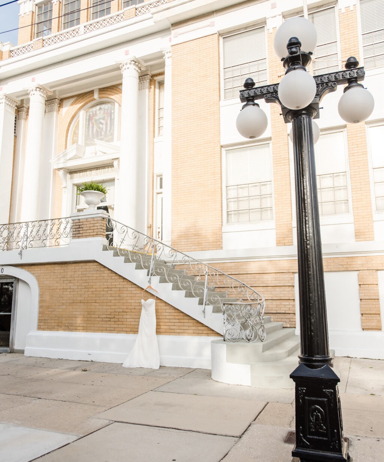 Elegant exterior of The Cuban Club featuring brick walls, white columns, and a staircase with a hanging wedding dress
