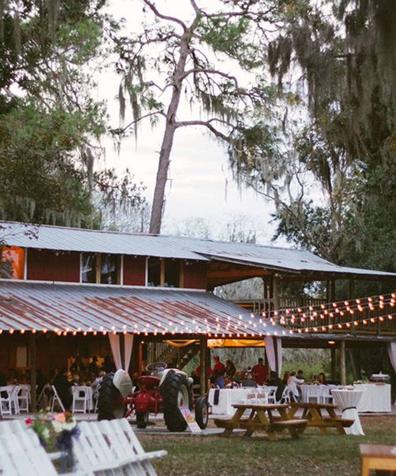 Rustic outdoor wedding reception with string lights, wooden tables, and a vintage tractor at Old McMicky’s Farm