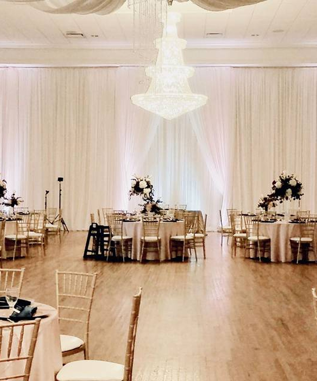 Elegant ballroom at The Regent with draped white walls, grand chandelier, round tables, and gold chiavari chairs
