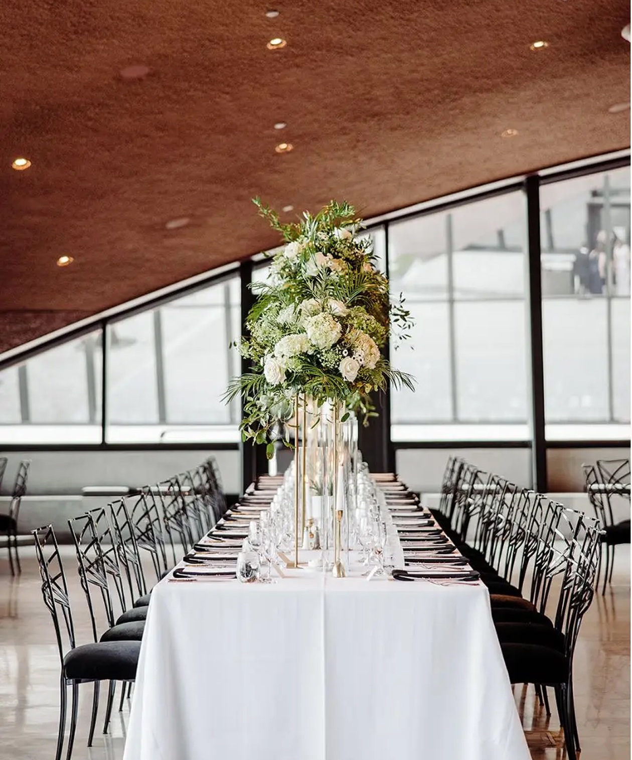 Long reception table with white linens and tall greenery centerpieces at Winter Park Events Center