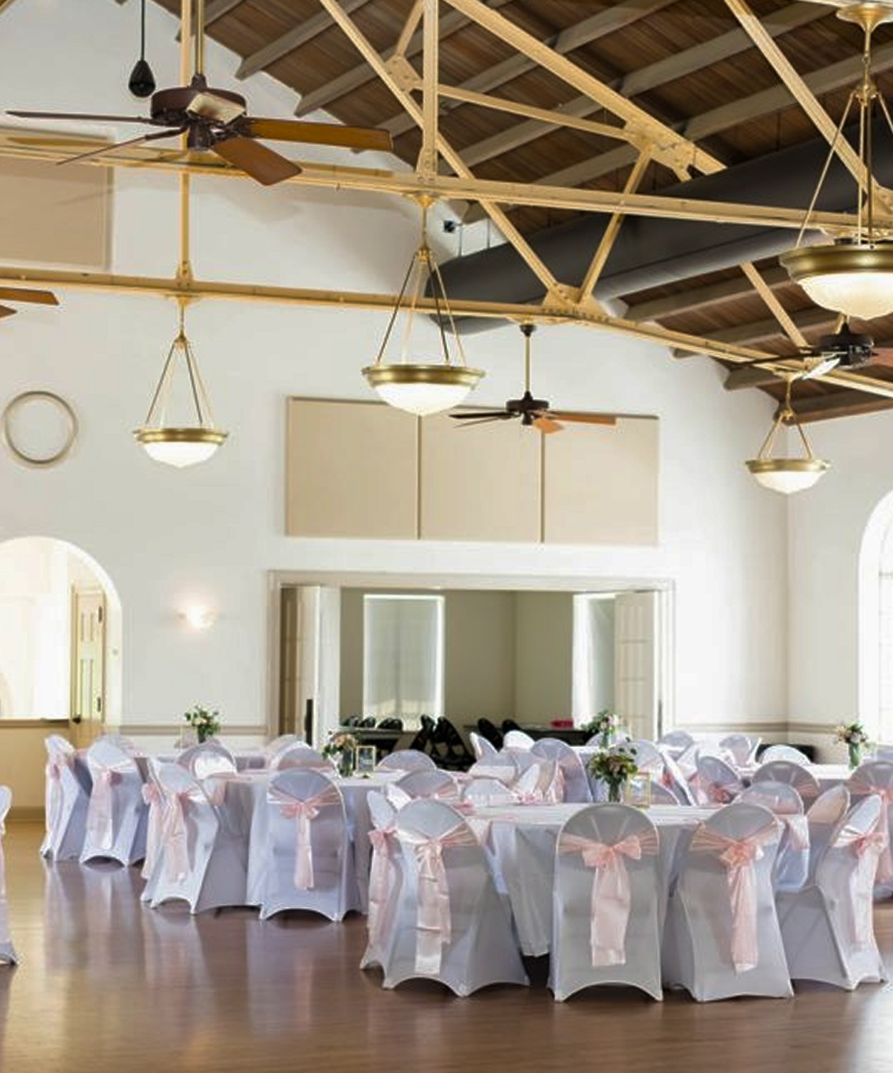 Wedding reception setup at the Magnolia Building with round tables, white chairs tied with pink bows, and natural light