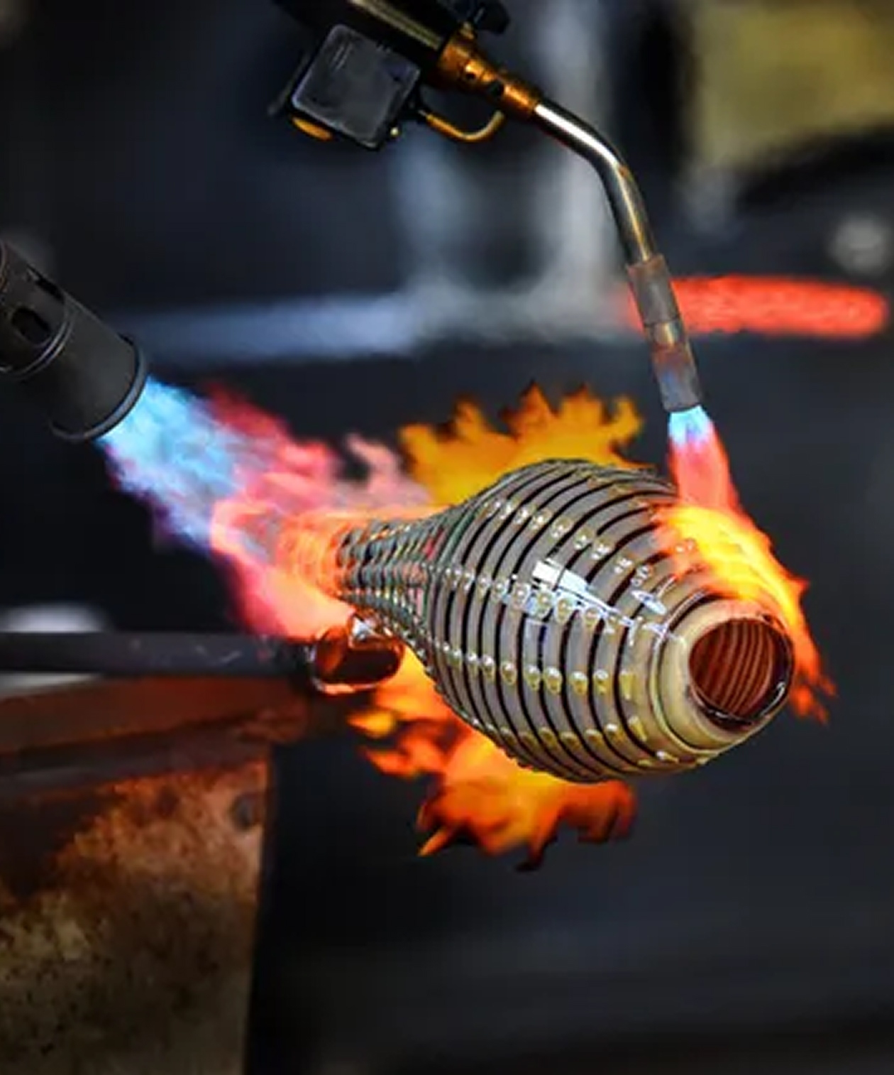 Glass artist shaping molten glass with dual torches at Morean Glass Studio & Hotshop, flames glowing around the piece