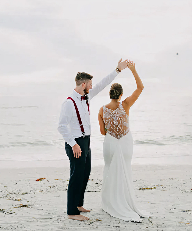 Bride and groom dancing barefoot on the shoreline at Lions Club Beach House, St. Petersburg, with soft waves behind them