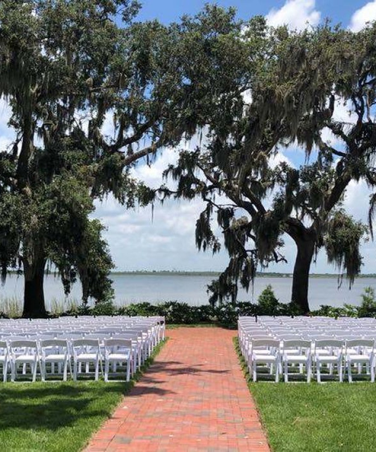 Outdoor wedding ceremony setup with white chairs and oak trees overlooking the lake at Adam’s Estate