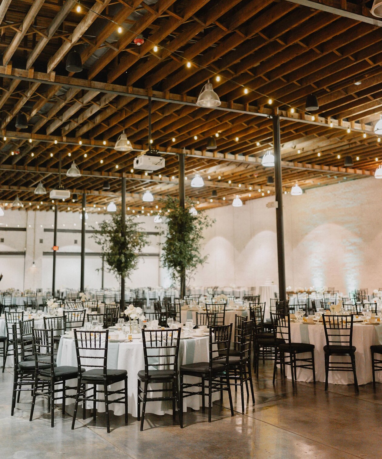 Modern wedding reception at Haus 820 with round tables, black chairs, string lights, and tall greenery accents