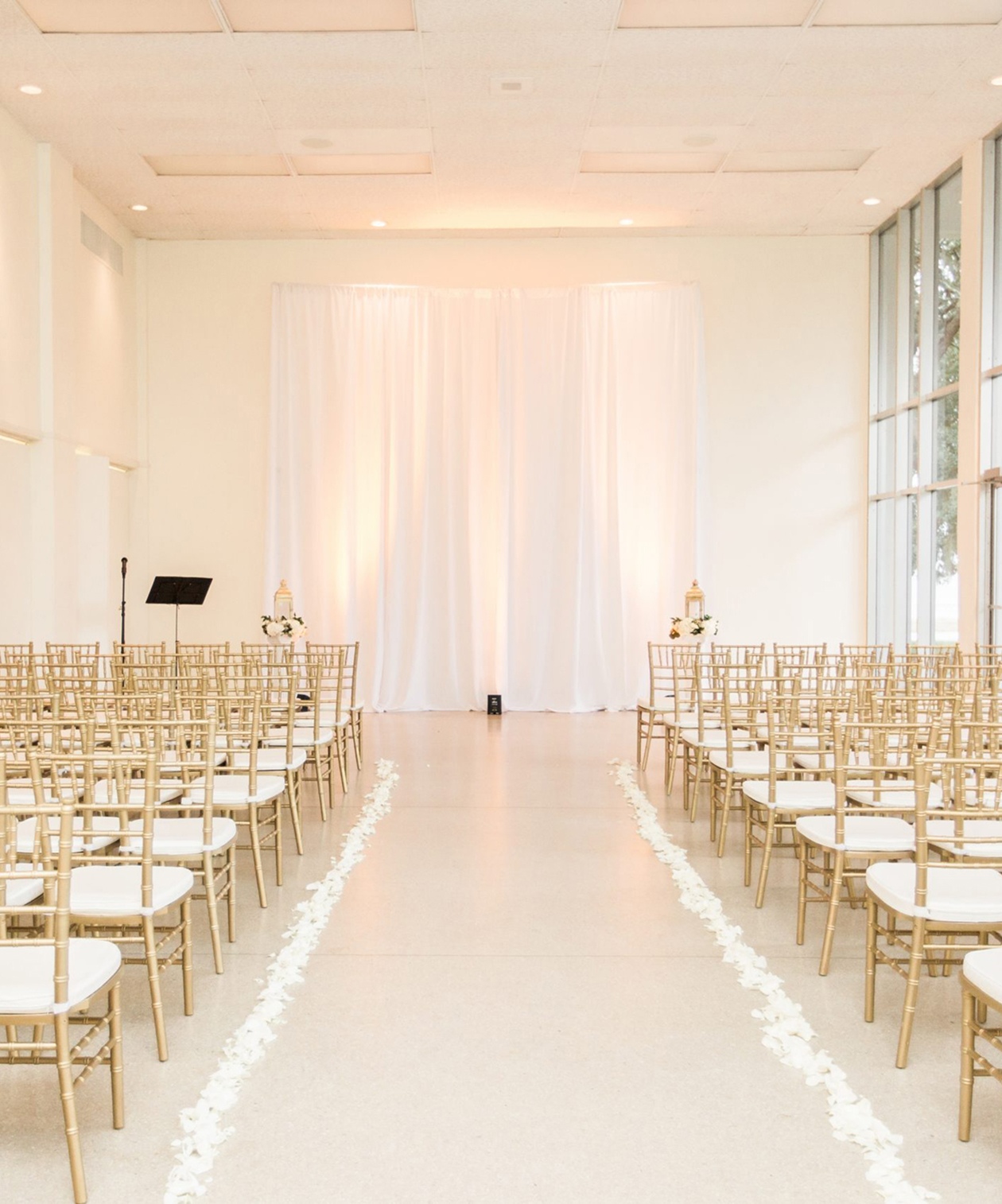 Elegant indoor ceremony setup at Tampa Garden Club with gold chairs, white drapery backdrop, and rose petal aisle