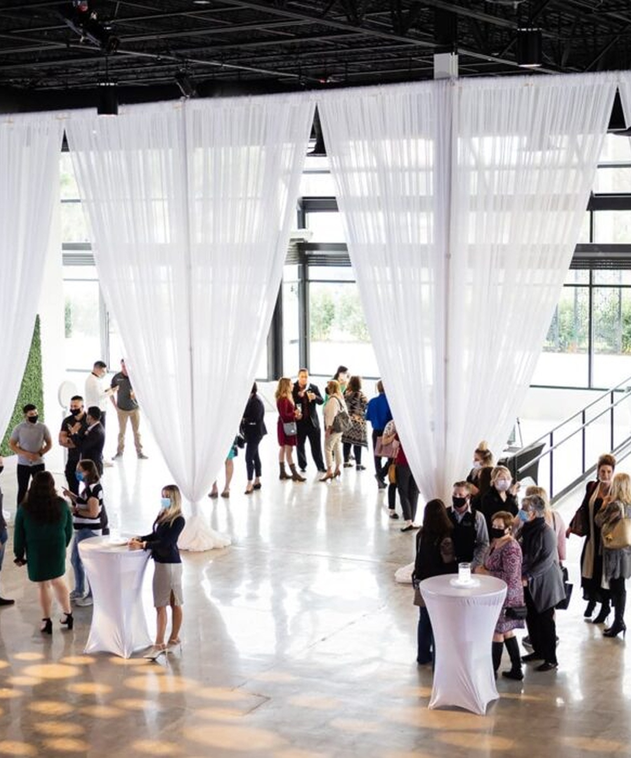 Guests mingling around cocktail tables beneath tall, flowing white drapery in the bright, modern Canvas Event Venue