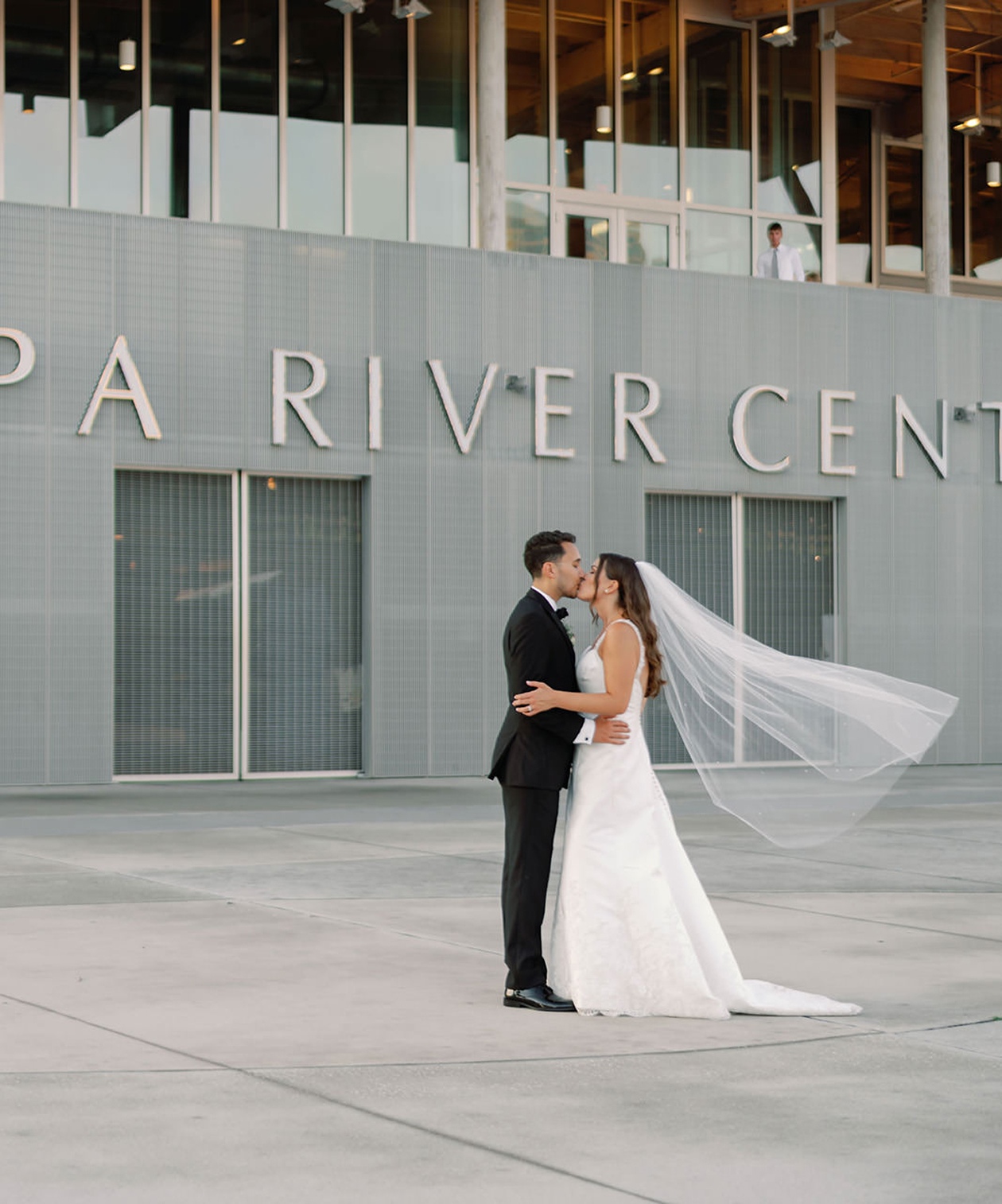 Bride and groom share a kiss outdoors in front of the modern gray exterior at Tampa River Center at Julian B Lane Park
