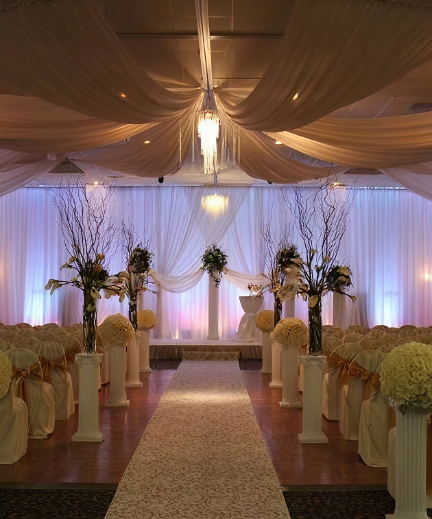 Elegant ceremony setup at Bayanihan Arts and Events Center with draped ceilings, white aisle runner, and floral columns