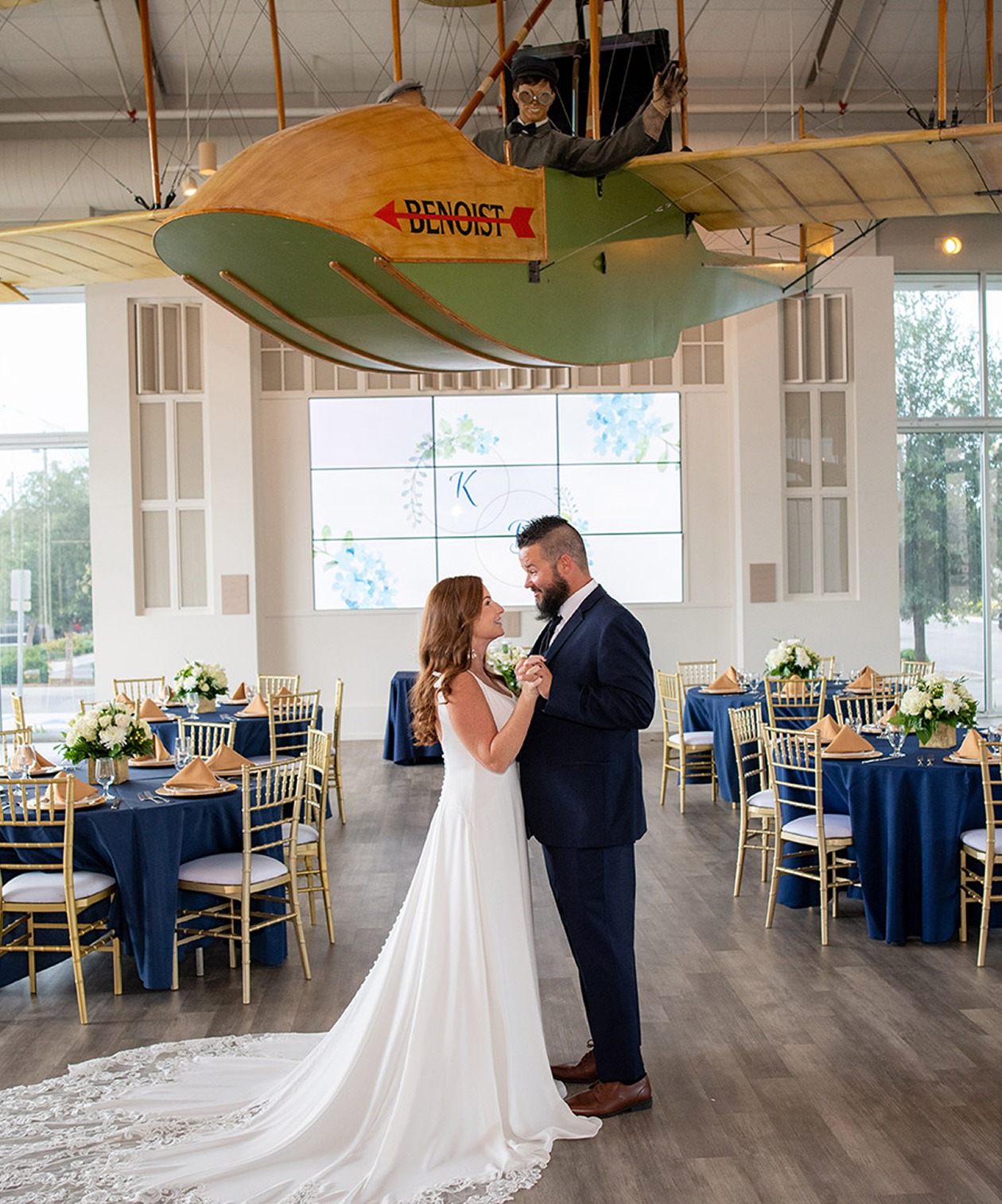 The Wedding couple dancing inside the St. Pete Museum of History, with an airplane display above and elegant navy decor.