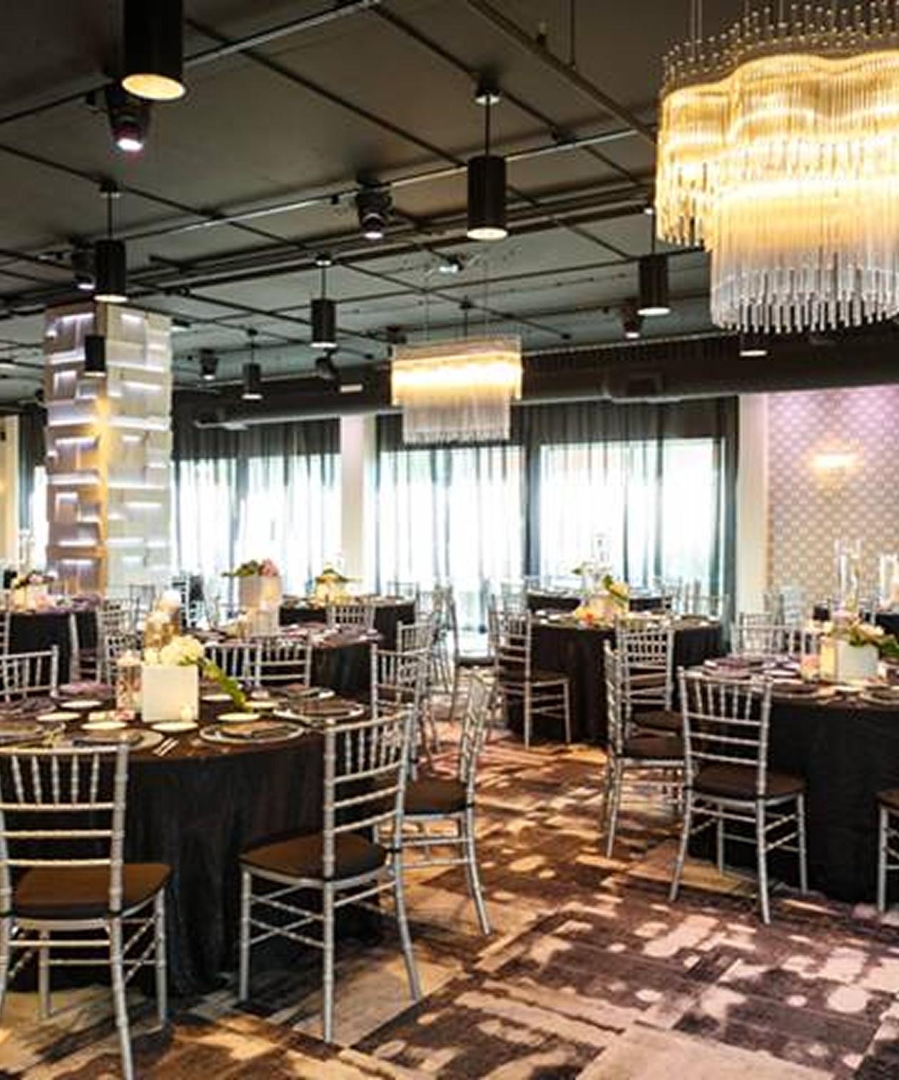 Elegant wedding reception setup at The MEZZ with round tables, silver chiavari chairs, and modern chandeliers overhead