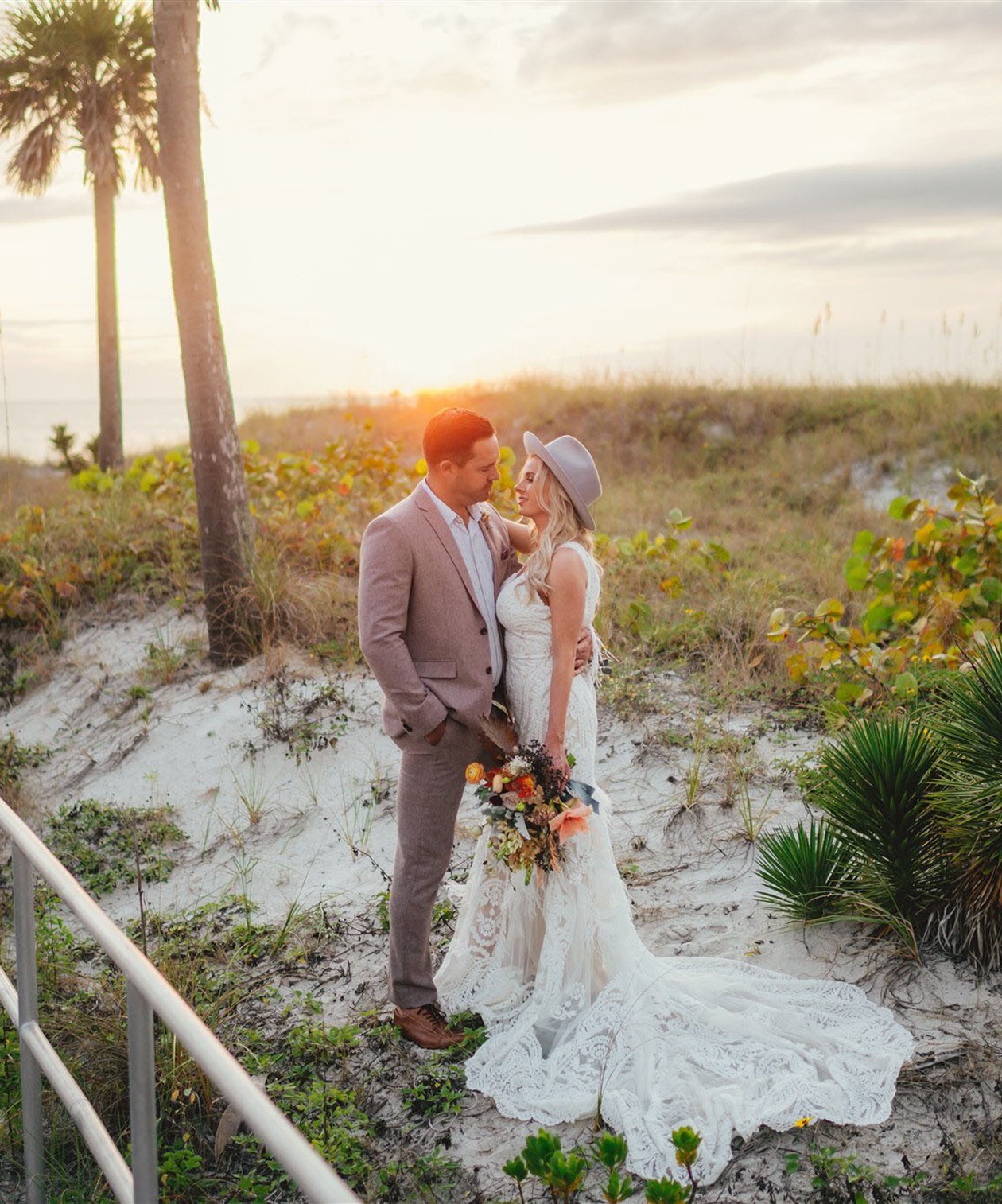 Couple posing at The West Events outdoor beach area during sunset, with palm trees and soft sand scenery