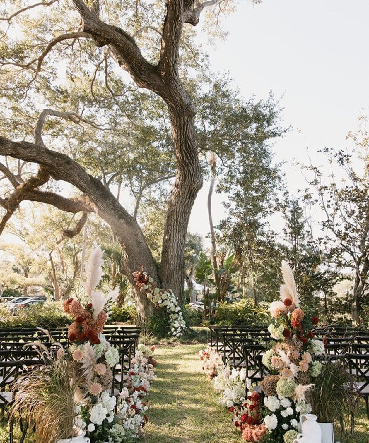 Outdoor ceremony setup at Victoria 1883 with lush florals, wooden chairs, and a large oak tree as the backdrop