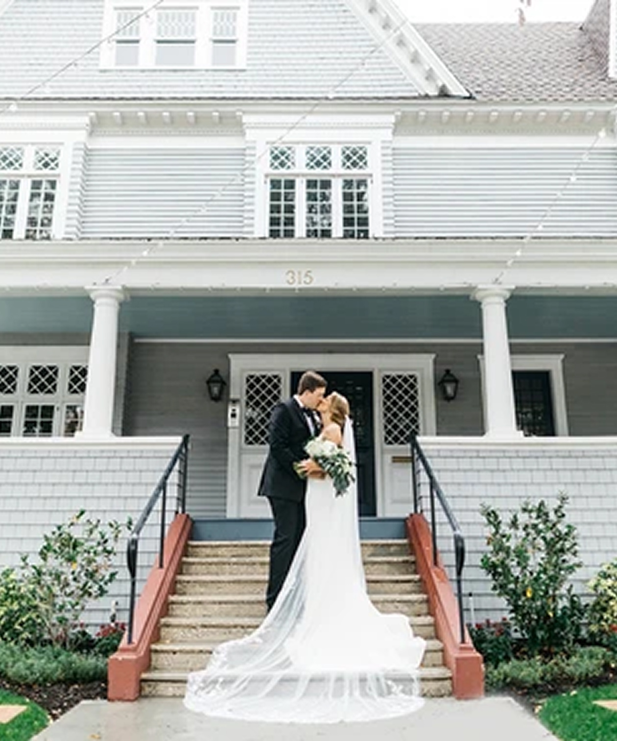 Bride and groom embrace on the front steps of The Orlo House & Ballroom, with historic white exterior as backdrop