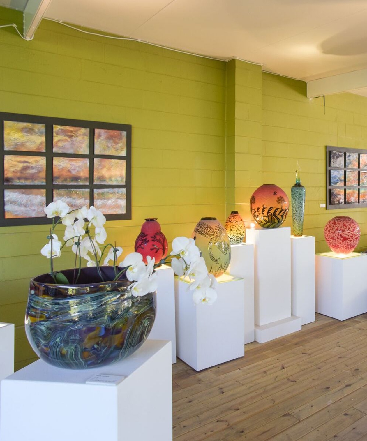 Art display at Duncan McClellan Gallery featuring hand-blown glass vases on white pedestals and orchids inside the vases