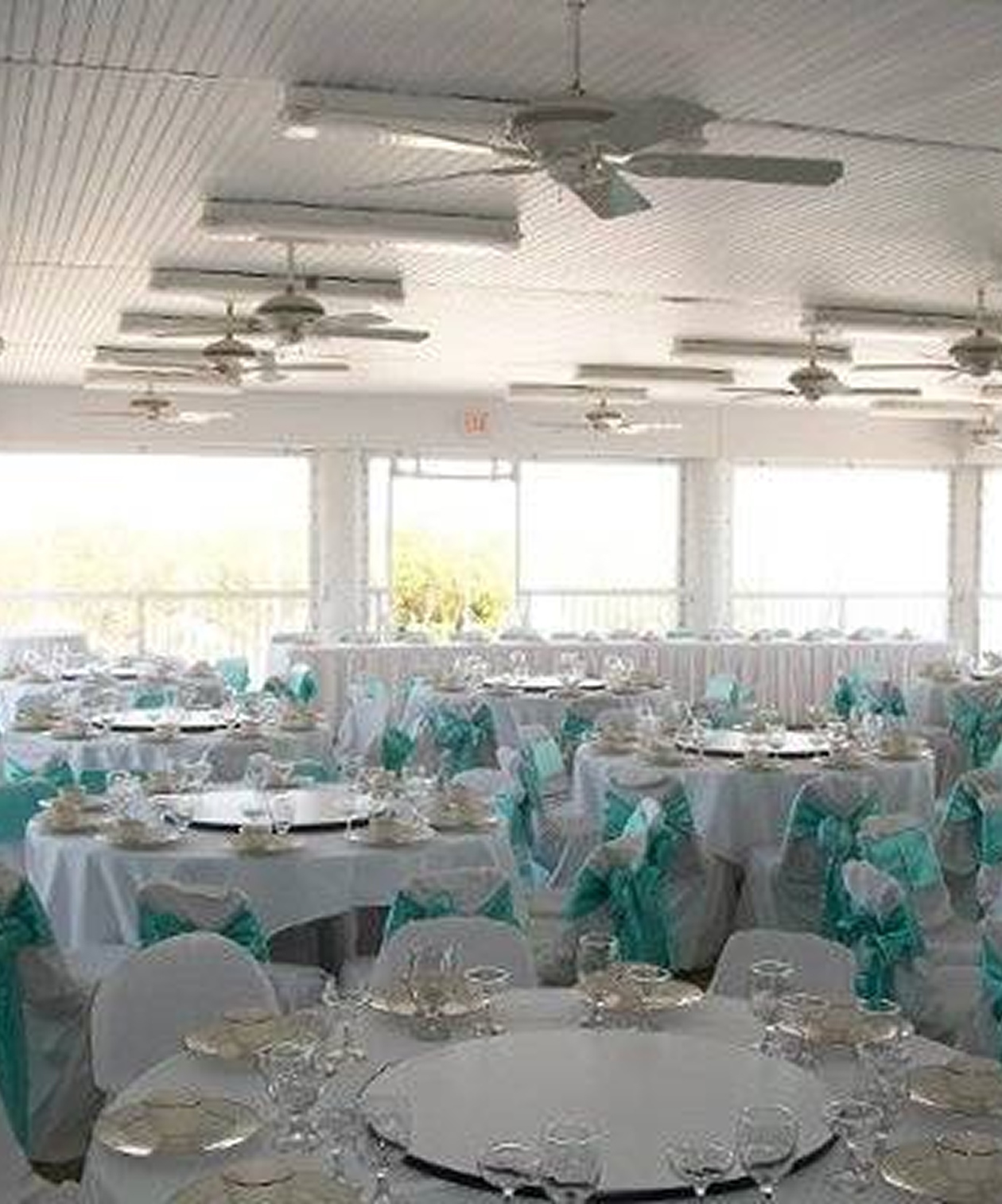 Wedding reception setup at Clearwater Community Sailing Center with white tables and teal chair sashes by large windows