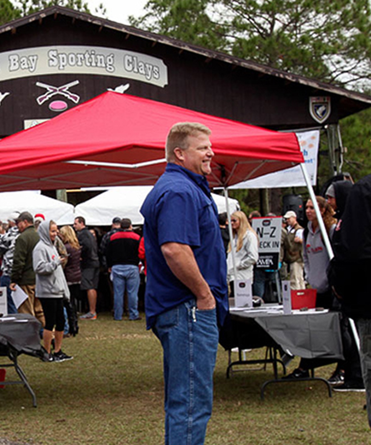Outdoor gathering at Tampa Bay Sporting Clays with guests under red tents, casual atmosphere, and event check-in area