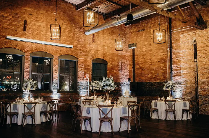 Industrial-style wedding reception with exposed brick walls, round tables, floral centerpieces and warm lighting