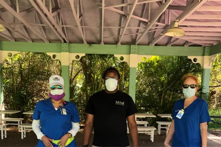 Three team members wearing masks standing under an outdoor pavilion, ready to provide safe service