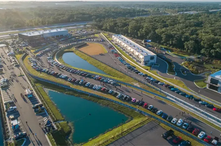 Aerial view of The Motor Enclave with winding tracks, parking areas, lakes, and surrounding greenery at sunset