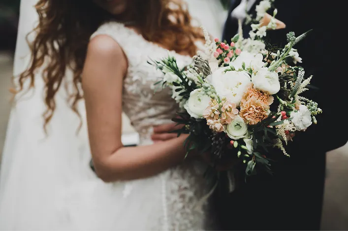 Close-up of a bride holding a romantic bouquet of white and blush flowers while standing beside the groom